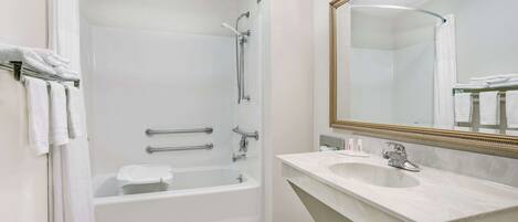 Un baño moderno con bañera, ducha y lavamanos, que cuenta con un espejo grande y azulejos blancos.