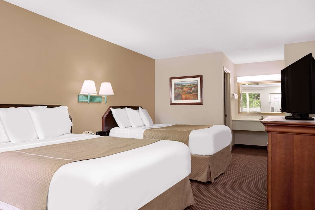 Ein Hotelzimmer mit zwei Betten, einem Schreibtisch, einem Fernseher und einem Gemälde an der Wand.