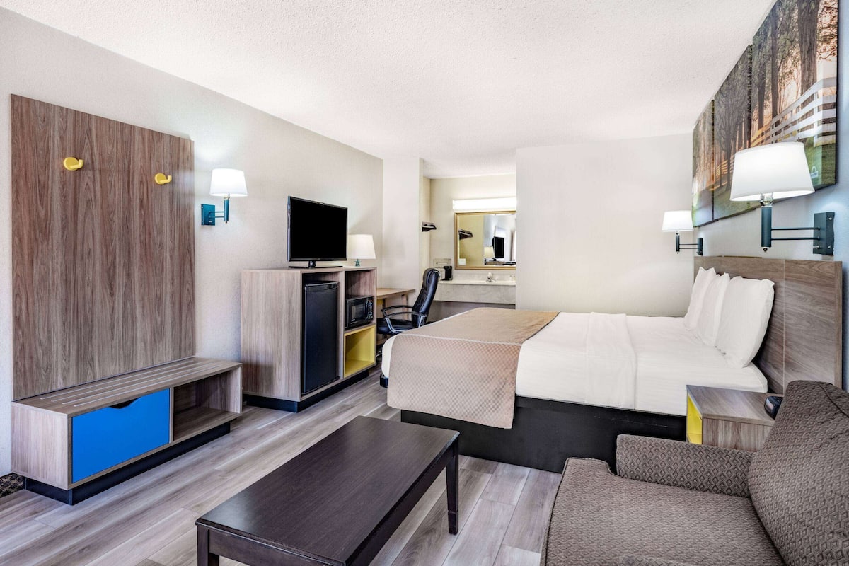 Ein Hotelzimmer mit Bett, Schreibtisch, Fernseher, Kleiderschrank und Spiegel.