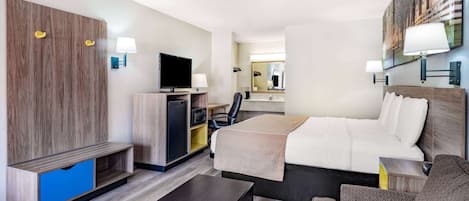 A hotel room with a bed, a desk, a television, a wardrobe, and a mirror.