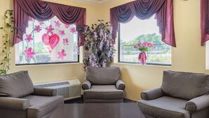 Una habitación con dos sillones, una mesita de centro y un amplio ventanal con cortinas decorativas y arreglos florales.