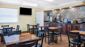 Un restaurante con mesas y sillas de madera, una zona de cocina y un televisor de pantalla plana en la pared.