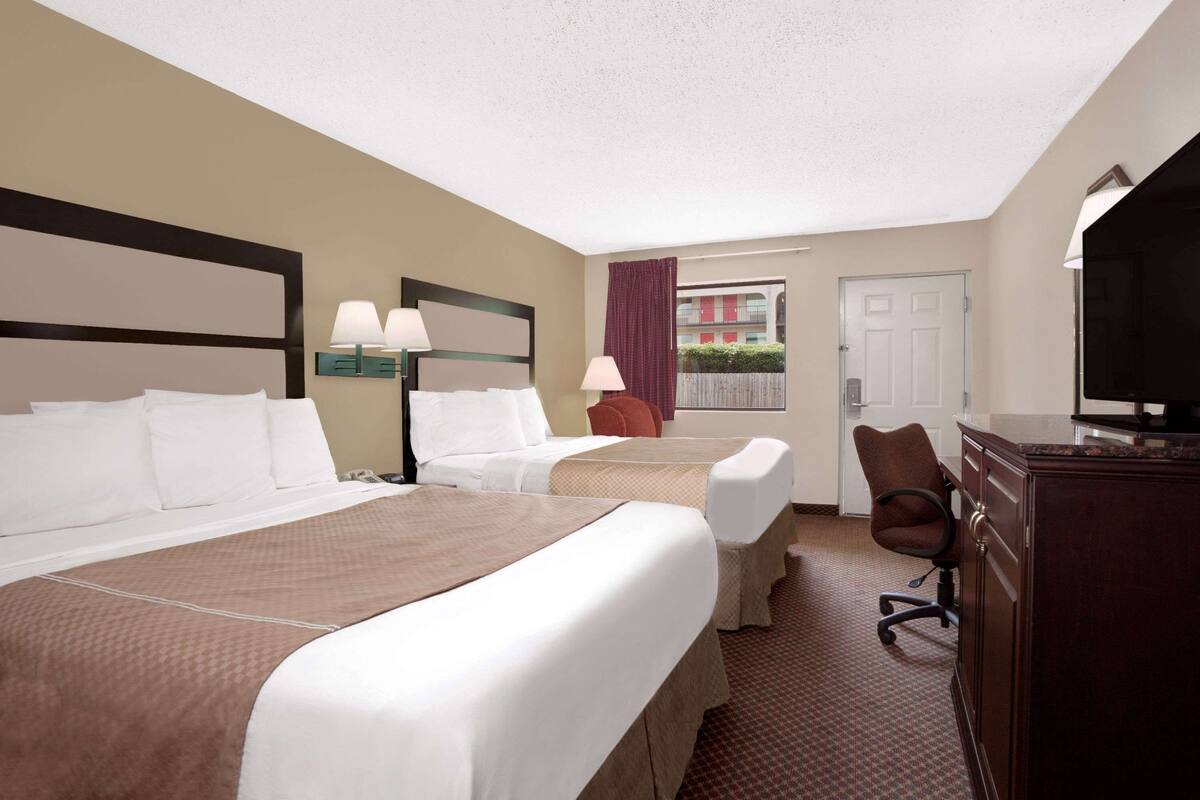Ein Hotelzimmer mit zwei Betten, einem Schreibtisch, einem Stuhl und einem Fernseher.
