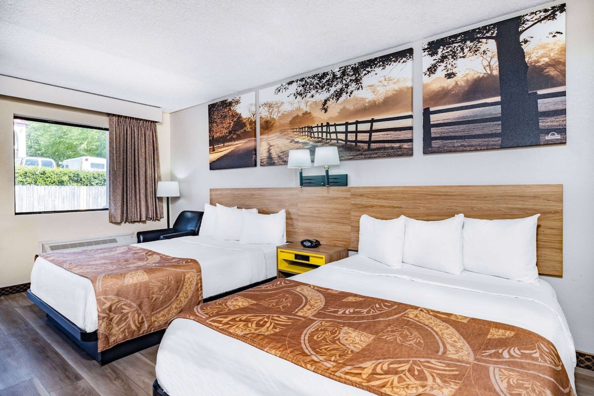 Ein Hotelzimmer mit zwei Betten, einem Schreibtisch, einem Stuhl, einer Lampe und einem Vorhangfenster.