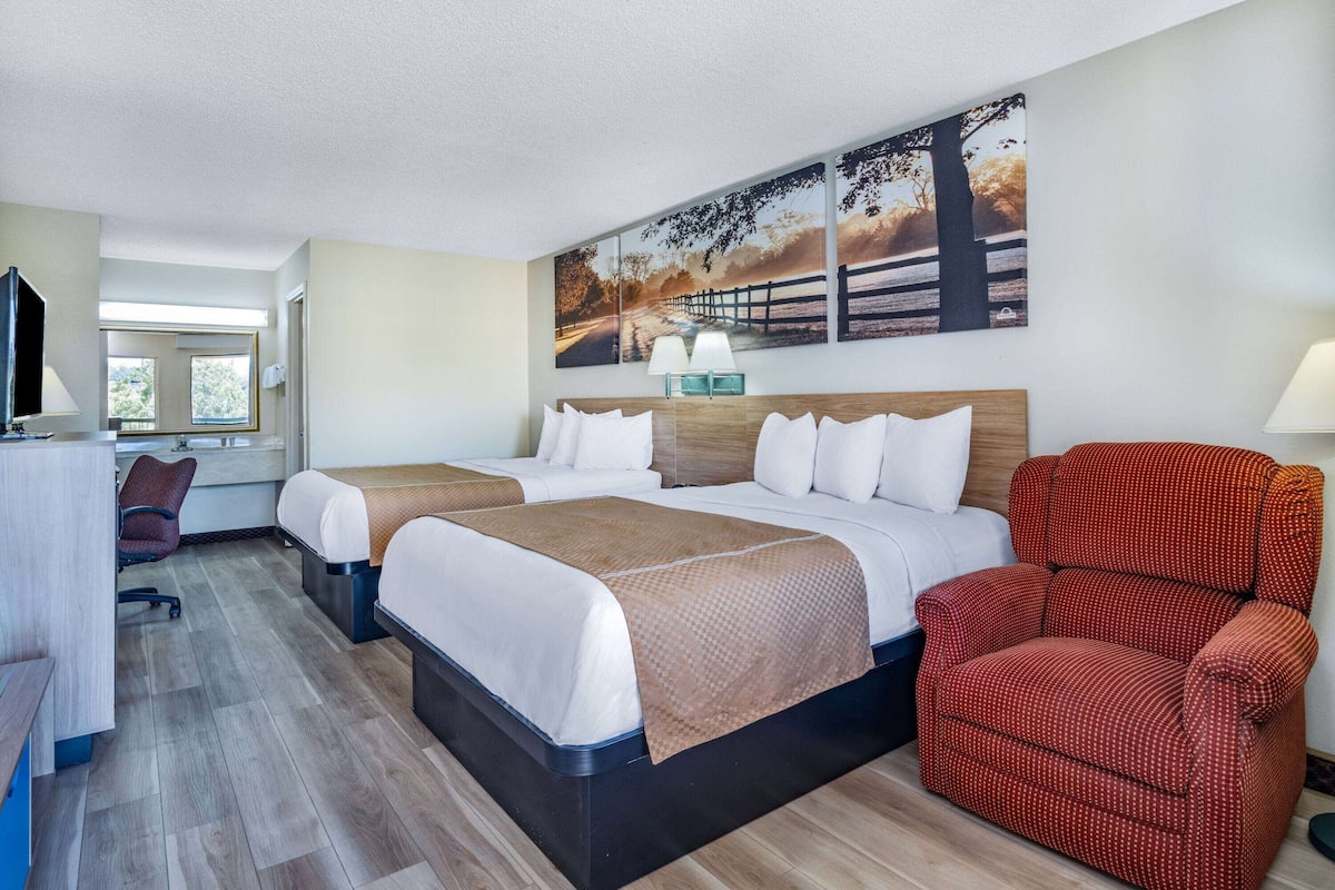 Ein Hotelzimmer mit zwei Betten, einem Schreibtisch, einem Stuhl und einem großen Fenster.