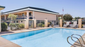 Un hotel con piscina, un patio cubierto y un área cercada con sillones de descanso.