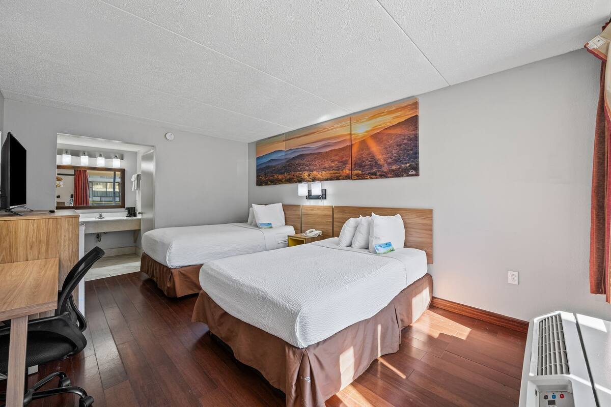 A hotel room with two beds, a desk with a chair, a TV, and a large painting on the wall.
