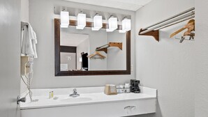 A modern bathroom with a white sink, a large mirror with lights, a towel rack, and a black chair. - Days Inn by Wyndham Nashville Saint Thomas West Hospital (Nashville)