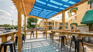 An outdoor deck with wooden tables and black bar stools, overlooking a street with parked cars and a building with a yellow facade. - Days Inn by Wyndham Nashville Saint Thomas West Hospital (Nashville)