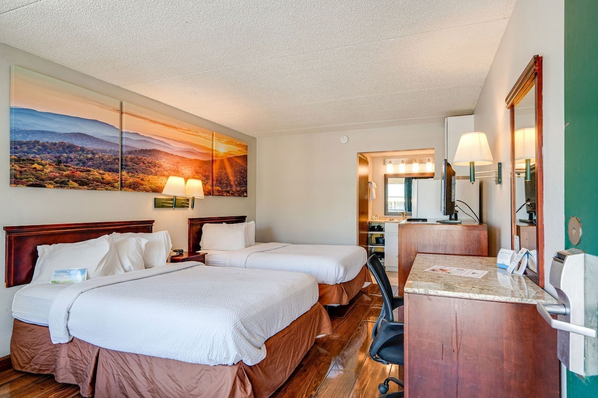 A hotel room with two beds, a desk, a mirror, and a painting of a landscape.