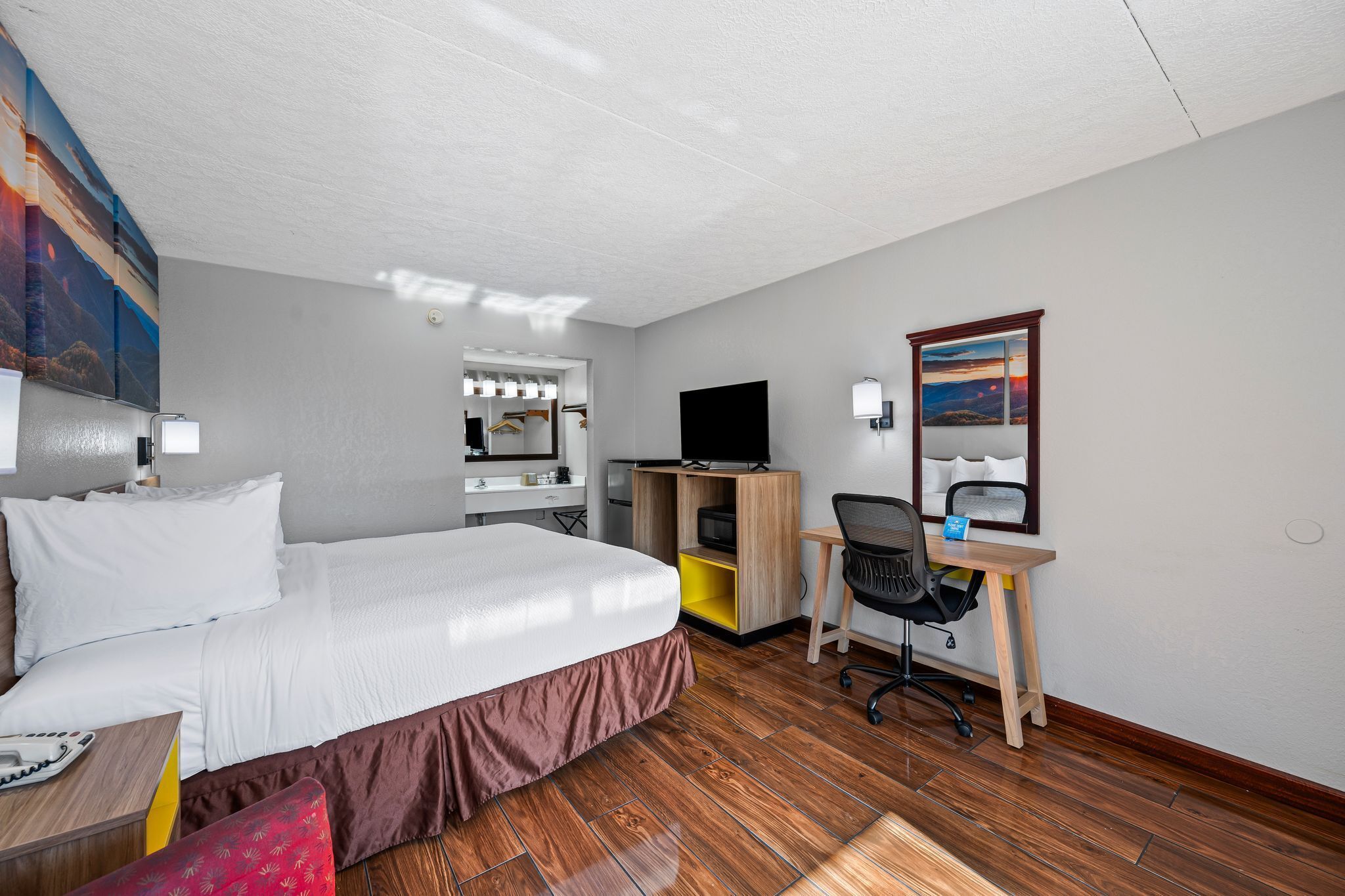 A hotel room with a bed, a desk, a chair, a TV, and a mirror.