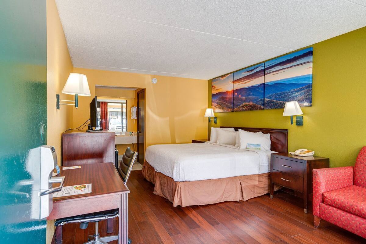 A hotel room with a bed, desk, chair, and a painting on the wall.