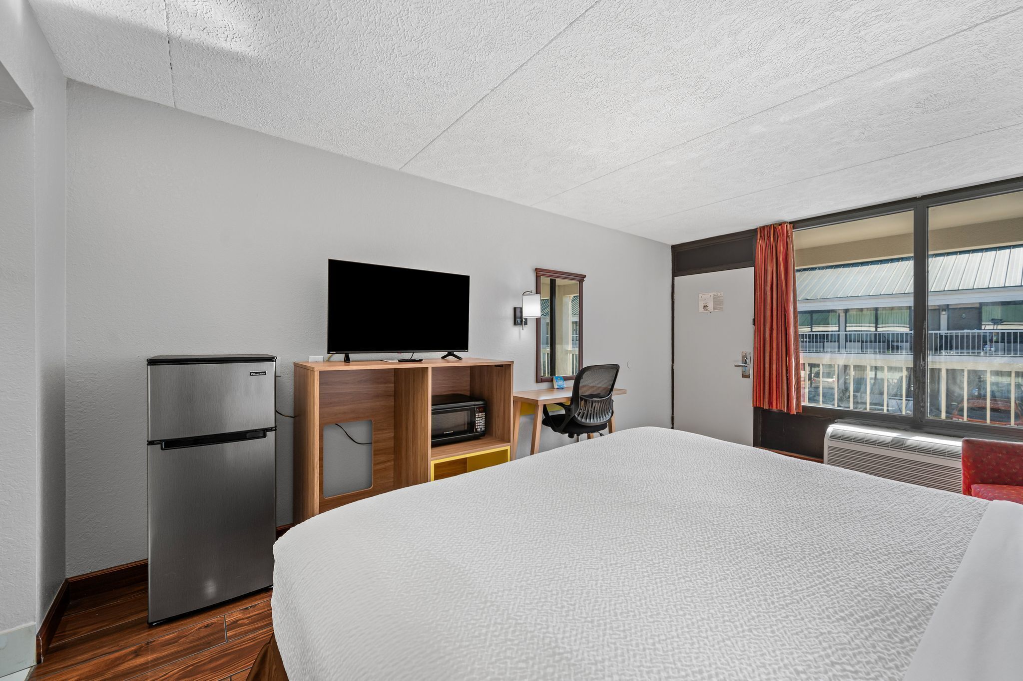 Habitación de hotel con cama, televisor de pantalla plana, refrigerador, microondas, escritorio y una silla.