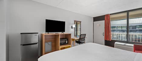 Habitación de hotel con cama, televisor de pantalla plana, refrigerador, microondas, escritorio y una silla.