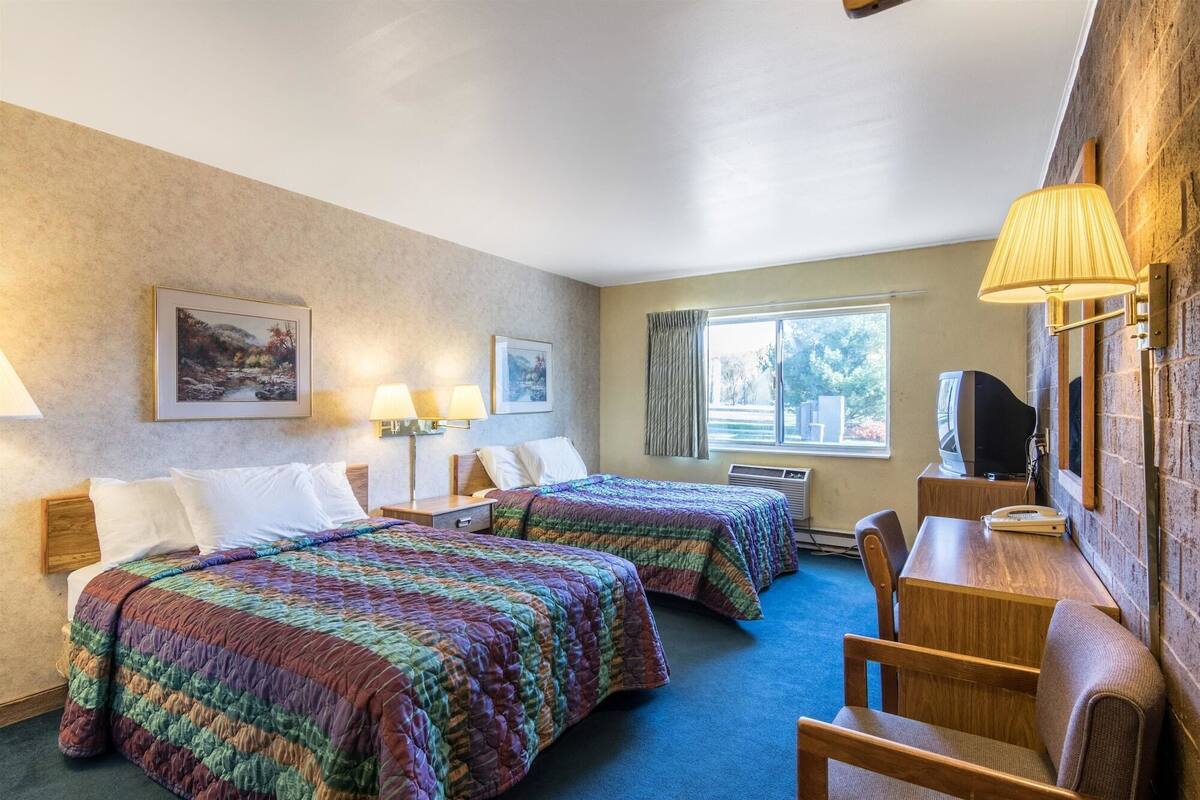 Hotelkamer met twee bedden, een bureau, een stoel, een televisie en een raam met gordijnen.