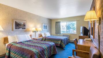 A hotel room with two beds, a desk, a chair, a television, and a window with curtains.