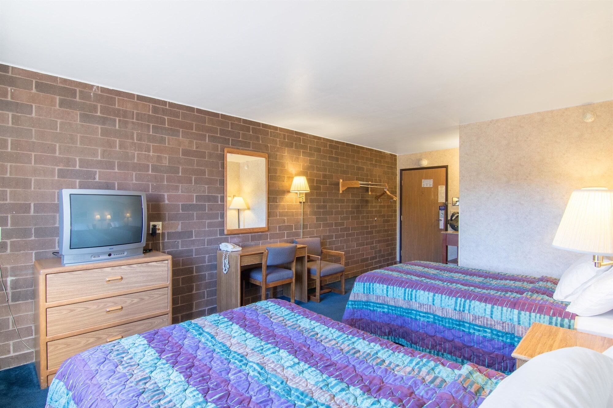 A hotel room with two beds, a desk, a chair, a television, and a mirror.