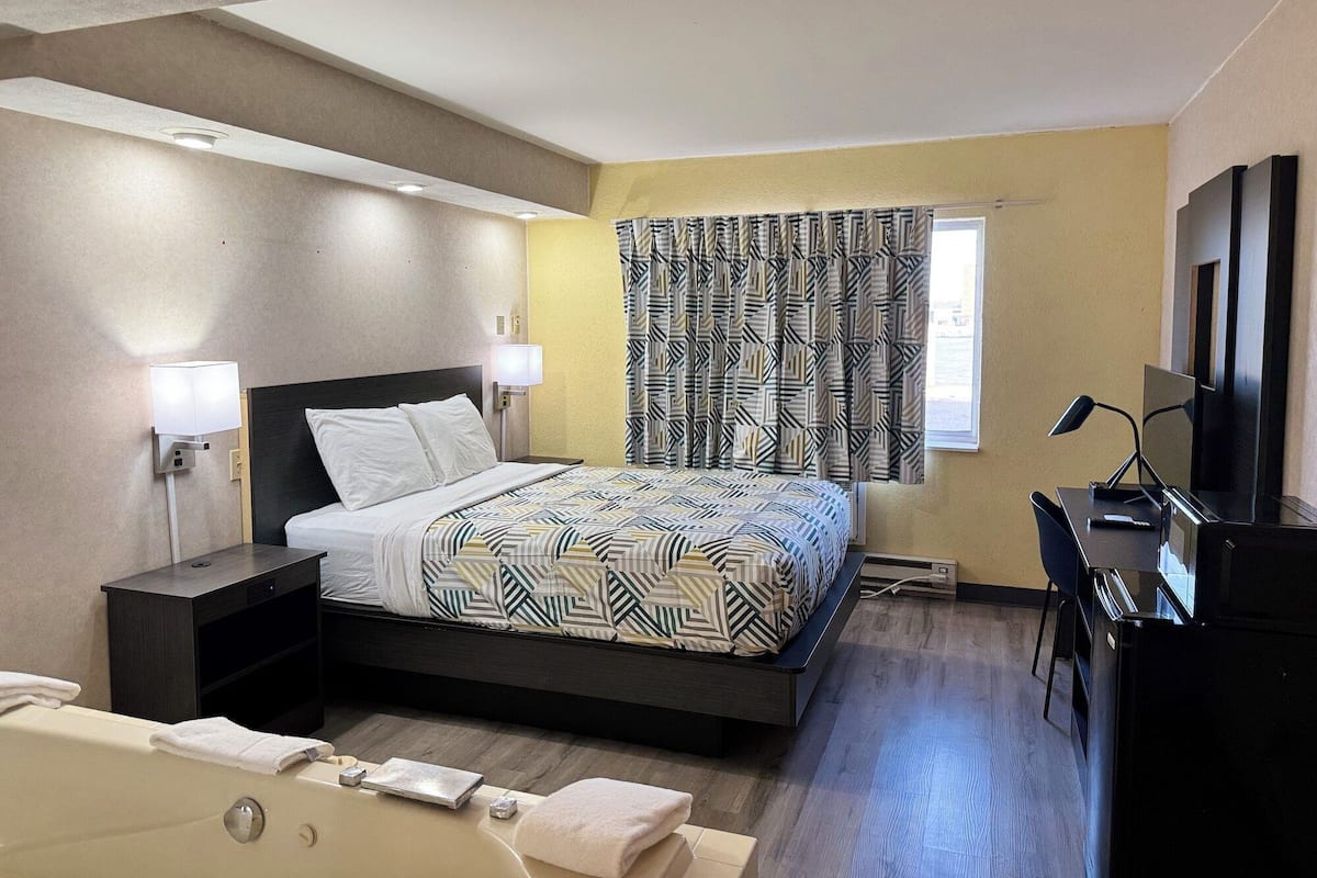 Een moderne hotelkamer met een bed, nachtlampjes, een bureau met een computer en een televisie.