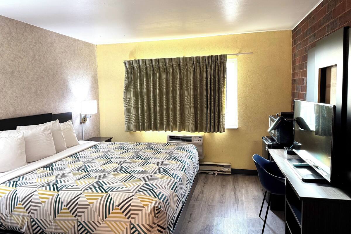 Een hotelkamer met een bed, een bureau, een stoel, een televisie en een raam met gordijnen.