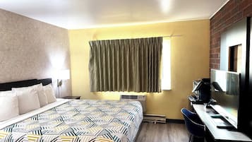 Una habitación de hotel con cama, escritorio, silla, televisión y ventana con cortinas.