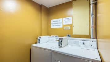 A laundry area with two washers and dryers, a caution sign, and a warning sign about currency acceptance.