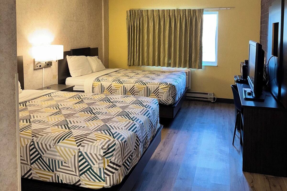 Een hotelkamer met twee bedden, een bureau met een computer en een raam met gordijnen.