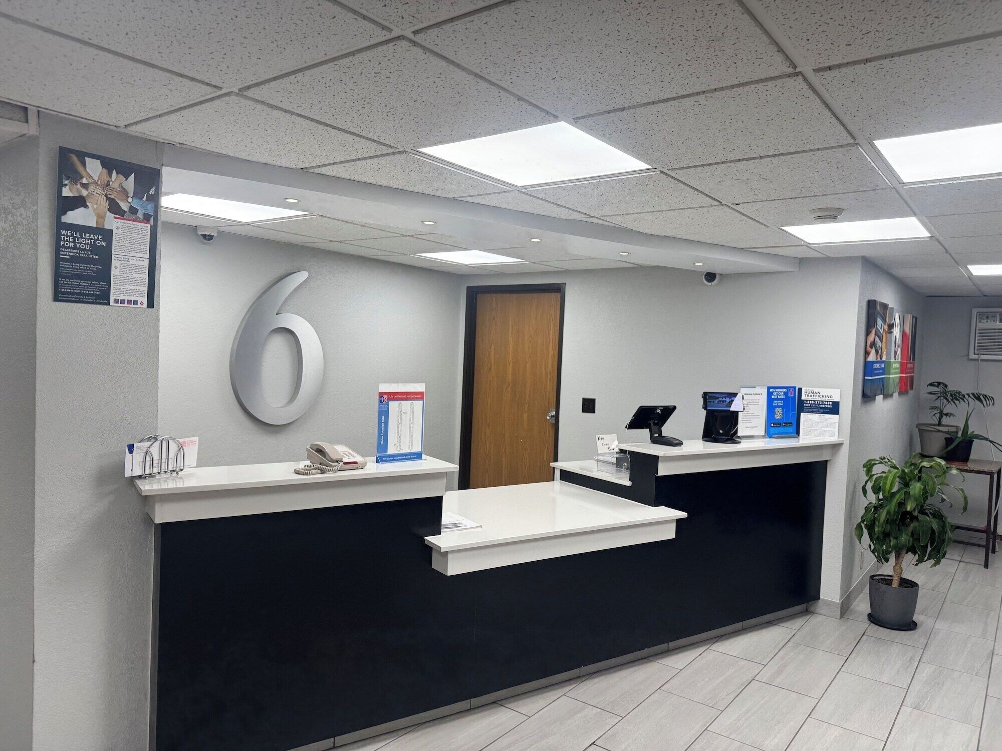 A reception desk with a large number '6' sign, a phone, a computer, and informational posters.