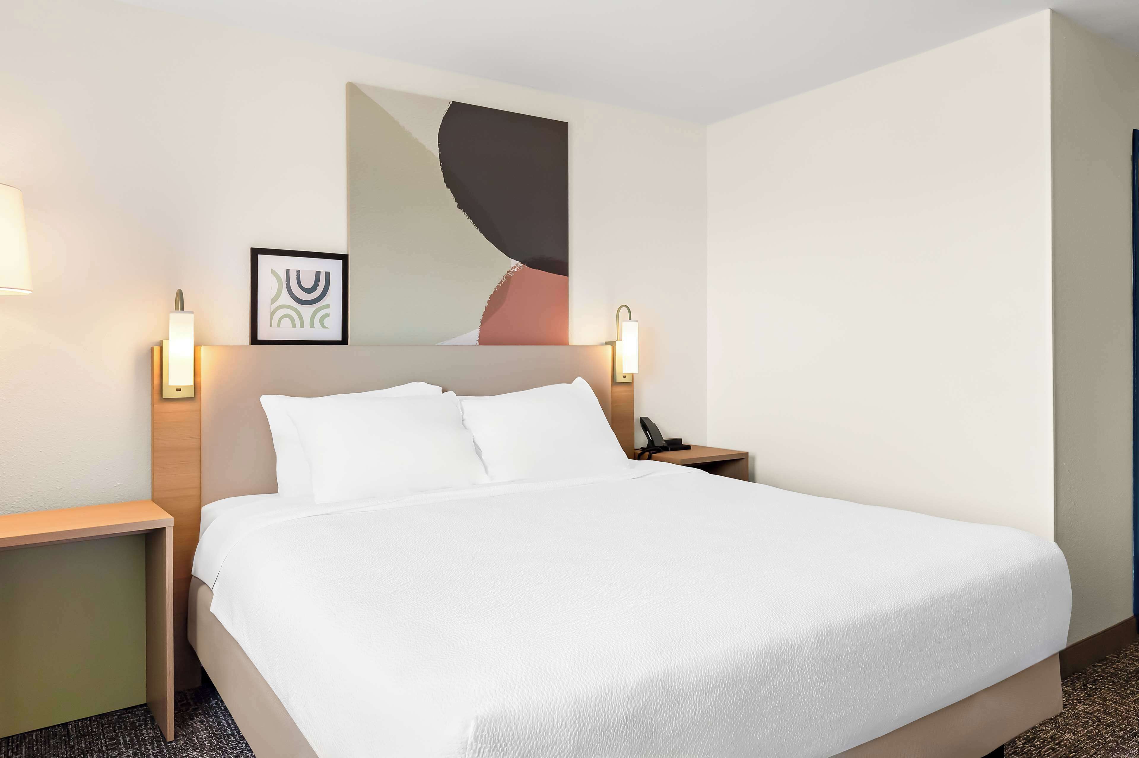 A hotel room with a large bed, two bedside tables, a nightstand, and a wall-mounted artwork.
