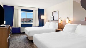 A hotel room with two beds, a desk, a chair, a window with curtains, and wall-mounted lamps. - Spark by Hilton Springfield Southwest (Springfield)