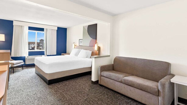 A hotel room with a large bed, a sofa, a desk, and a window with curtains. - Spark by Hilton Springfield Southwest (Springfield)