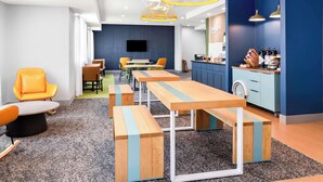 A modern meeting room with wooden tables and benches, a kitchen area, and a seating area with orange chairs. - Spark by Hilton Springfield Southwest (Springfield)