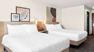 A hotel room with two beds, a wooden headboard, bedside tables with lamps, and framed artwork on the wall.