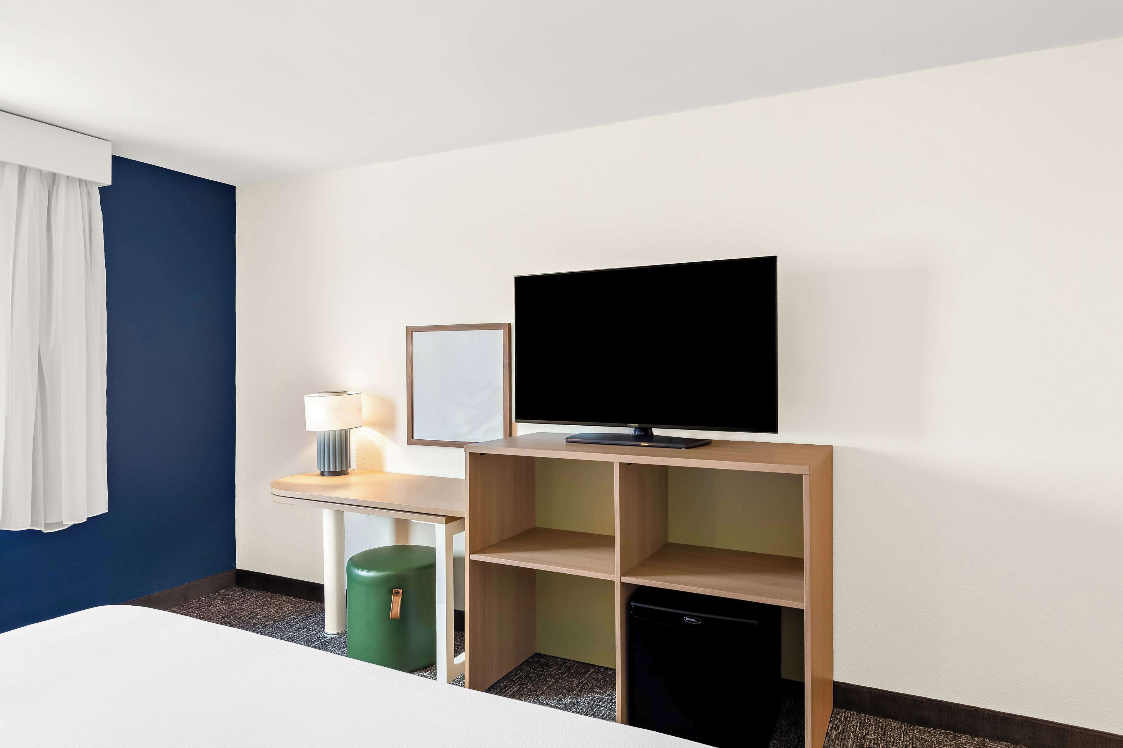 Een hotelkamer met een bed, een bureau met lamp, een televisie en een prullenbak.