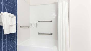 A modern bathroom with a white bathtub, two handrails, and a towel rack.
