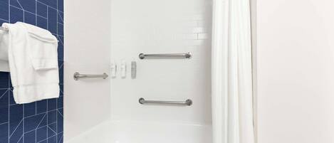 A modern bathroom with a white bathtub, two handrails, and a towel rack.