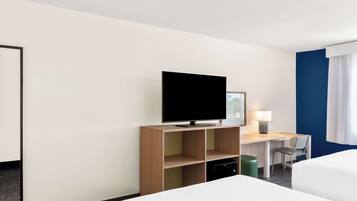 A hotel room with a bed, a desk with a flat-screen TV, a chair, a lamp, and a trash bin.