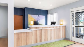 A reception desk with a wooden finish, a large abstract painting, and a glass door with a patterned view. - Spark by Hilton Springfield Southwest (Springfield)
