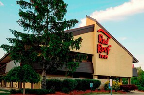 Ein Red Roof Inn Gebäude mit einem geneigten Dach und einem großen Baum davor.