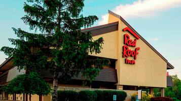 Edificio de Red Roof Inn con techo inclinado y un gran árbol en primer plano.