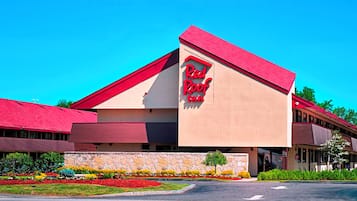 A Red Roof Inn with a red roof and beige walls, surrounded by a landscaped garden with colorful flowers.