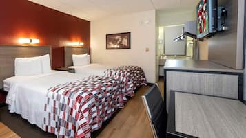 Habitación de hotel con dos camas, un escritorio, televisión y baño visible a través de una puerta abierta.