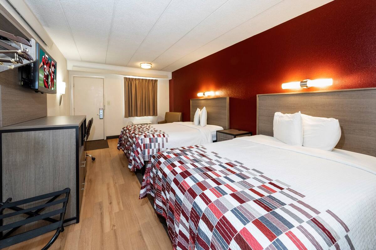 A hotel room with three beds, a desk, and a TV.