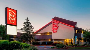 Un hôtel Red Roof Inn reconnaissable à son grand panneau néon, doté d’une façade moderne et d’un aménagement paysager bien entretenu.