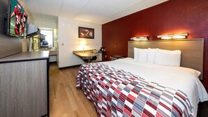 Une chambre d’hôtel comprenant un lit, un bureau, une chaise, une lampe, un téléviseur et un luminaire fixé au mur.