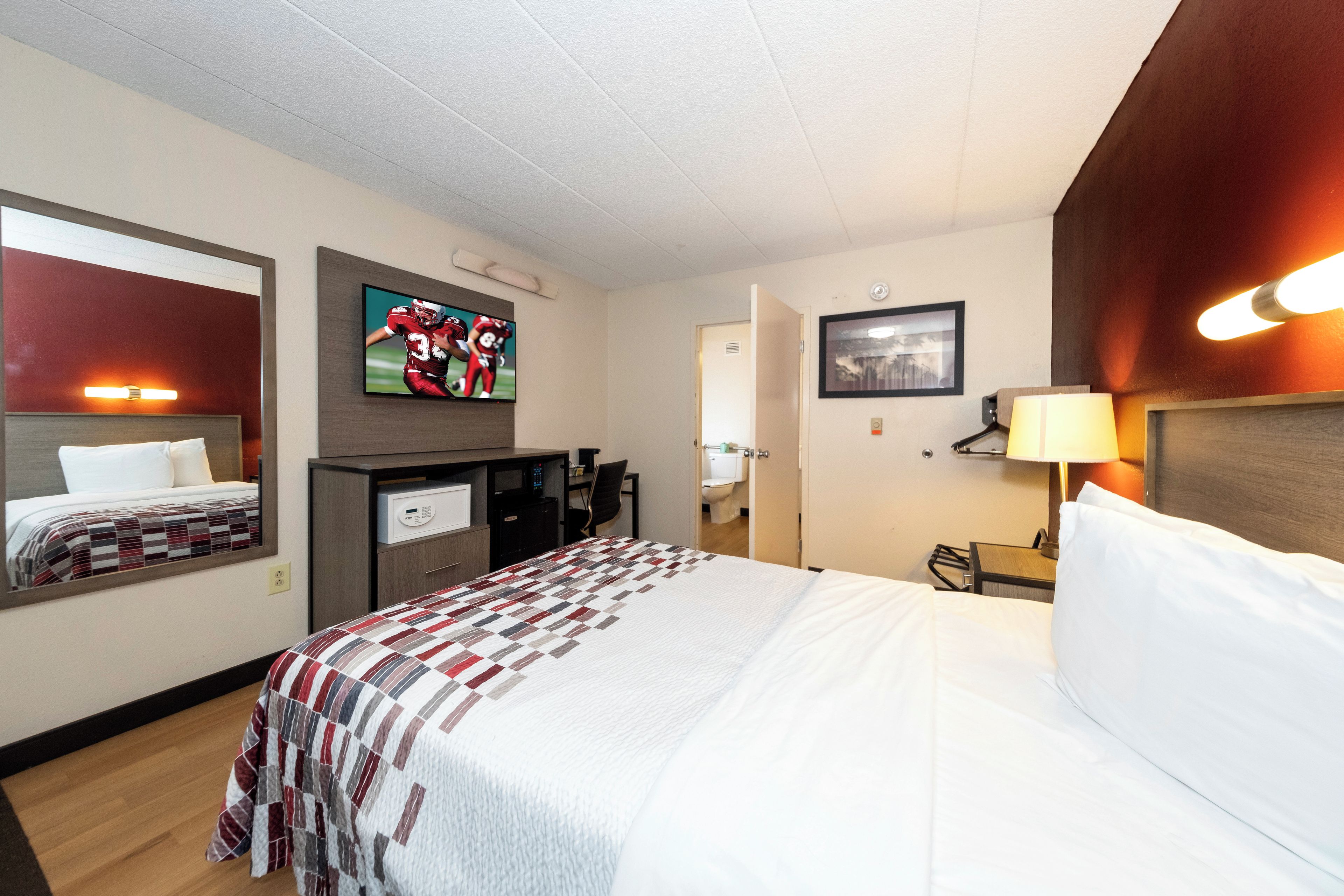 Quarto de hotel com cama, escrivaninha, televisão e banheiro visível por uma porta aberta.