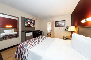 Quarto de hotel com cama, escrivaninha, televisão e banheiro visível por uma porta aberta.