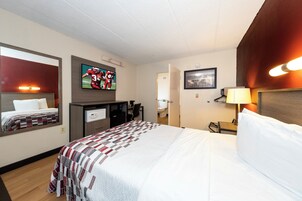 Habitación de hotel con una cama, un escritorio, un televisor y un baño visible a través de una puerta abierta.