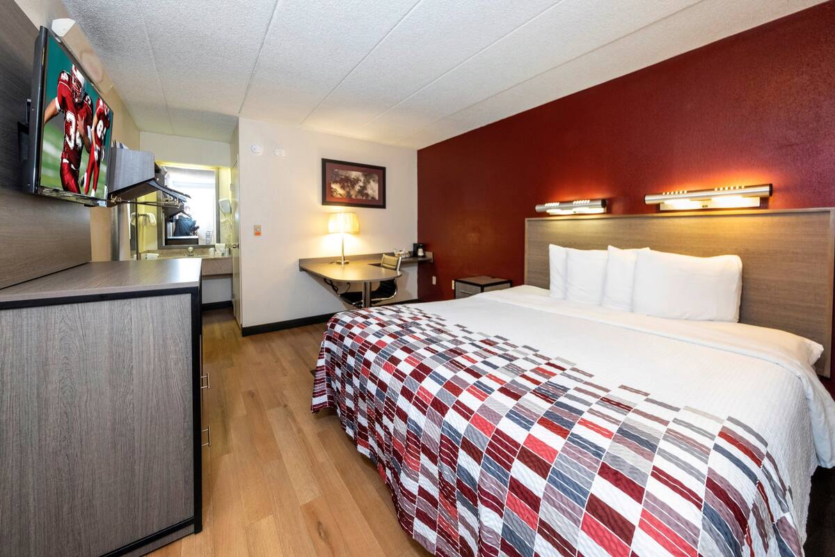 A hotel room with a bed, a desk, a chair, a TV, and a lamp.