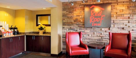 Vestíbulo de Red Roof Inn con una pared de piedra, una estación de café y dos sillones de cuero rojo.