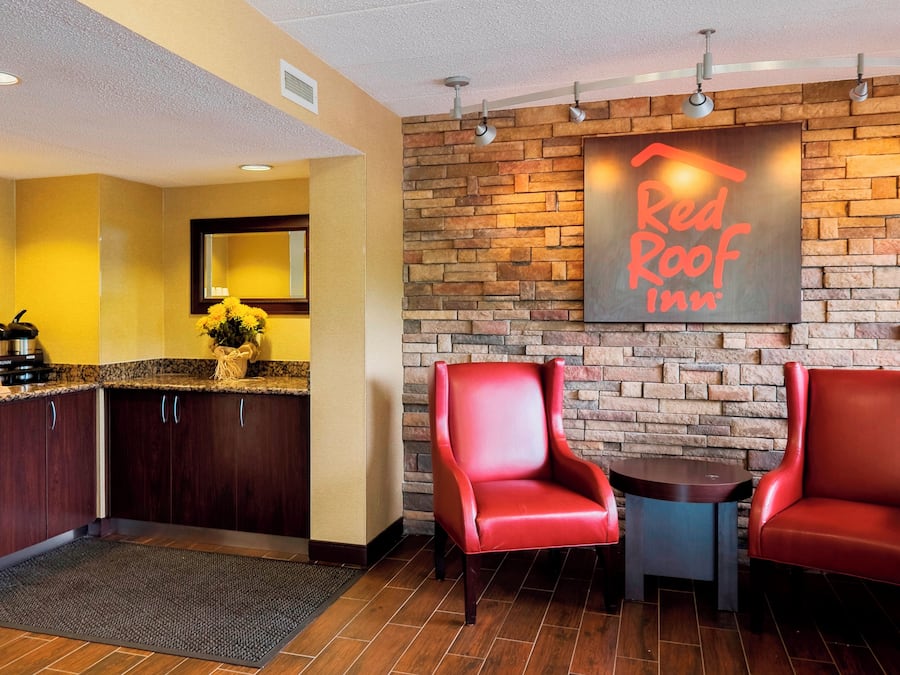 A Red Roof Inn lobby with a stone wall, a coffee station, and two red leather chairs.